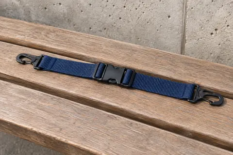 Petite sangle de poitrine bleu marine avec boucle centrale et crochets d’attache, posée seule sur un banc en bois