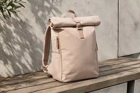 Sac à dos roll-top beige rosé posé sur un banc, avec sa face avant souple et ses rangements visibles.