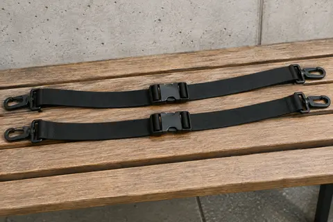 Deux longues sangles de poitrine noires à boucle à dégagement rapide, posées en courbes parallèles sur un banc en bois