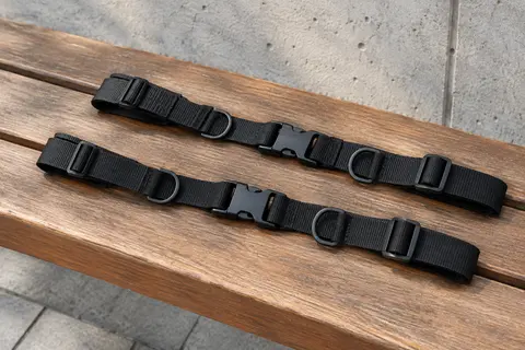 Deux sangles de poitrine noires réglables avec boucle rapide et anneaux en D, posées sur un banc urbain.