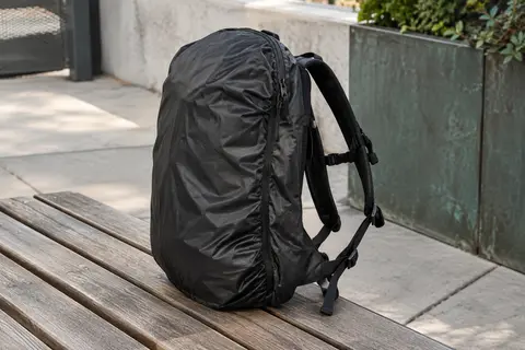 Housse de pluie noire ajustée sur un petit sac à dos posé sur un banc en bois en ville.